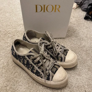 Dior sneakers med monogram - Säljer ett par snygga Dior sneakers med klassiskt blått och vitt monogrammönster. Skorna har snörning och vit platt sula med stjärndetalj undertill. lite slitna i hälarna. box medföljer. öppen för byten och pris går att diskutera🥰