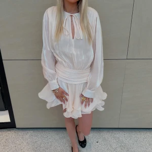 Vit fest klänning - Supersöt vit klänning med omlottkänsla, volangdetaljer och knyt i halsen. Långa ärmar och markerad midja ger en feminin siluett. Perfekt för sommarens alla tillfällen! Storlek s/m men känns som s. Prislapp kvar. En knapp på ärmen har ramlat av💗 ja kan skicka bild på det privat