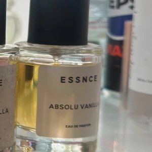 ESSNCE Absolu Vanilla Eau de Parfum - En stilren parfymflaska med svart lock och transparent glas som visar den gyllengula vätskan. Doften heter Absolu Vanilla och är en Eau de Parfum, perfekt för dig som älskar varma och söta vaniljtoner.
