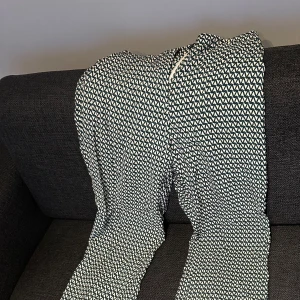 Mönstrade byxor från H&M - Säljer ett par snygga byxor från H&M med grafiskt mönster i grönt och vitt. Byxorna har normal passform och dragkedja i sidan. Perfekta för dig som vill sticka ut med ett coolt mönster.