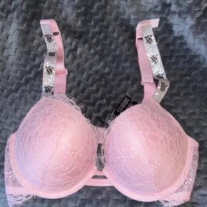 Victoria's Secret BH - Säljer en ljusrosa bh från Victoria's Secret med spetsdetaljer och glittriga axelband med VS-logga. Aldig använd. Nypris: 900kr