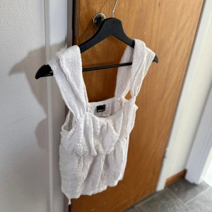 Vit linnetopp från Gina Tricot - Säljer en vit linnetopp från Gina Tricot med breda axelband och rynkad struktur. Toppen har en luftig och somrig känsla, perfekt för varma dagar. Materialet är lätt och toppens design är enkel men trendig.