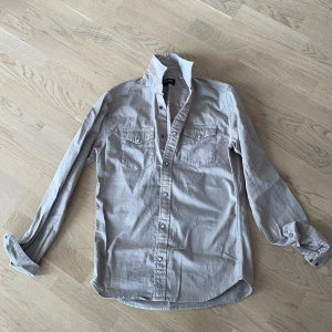 Beige skjorta från Jack & Jones - Säljer en beige skjorta från Jack & Jones med klassisk krage och två bröstfickor med knappstängning. Skjortan har långa ärmar och är tillverkad i ett mjukt bomullsmaterial. Perfekt för en stilren och avslappnad look.