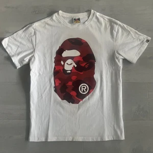Bape T-Shirt - Riktigt fet vit bape t shirt med rött tryck i storlek L men passar även M! Välanvänd men fortfarande i bra skick🙌 Mer frågor privat!