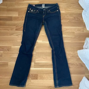 Mörkblå low waist bootcut jeans  - Säljer ett par lågmidjade mörkblåa byxor från True Religion. Säljer pga att jag inte anväder de längre. De har snygga bakfickor (se bild 3). De är i storlek 26. Jag är 174 och de passar mig perfekt i längden. 