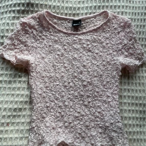 Ljusrosa spetsblus från Gina Tricot - Säljer en ljusrosa blus från Gina Tricot i storlek XS. Blusen är helt täckt av vacker spets och har korta ärmar. Perfekt för dig som gillar romantisk och feminin stil.