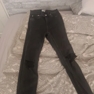 Svarta jeansbyxor från 157 - Svarta jeansbyxor från 157 i storlek M. Högmidjade med skinny passform och slitna detaljer vid knäna för en cool look. Klassisk femficksmodell med knapp och dragkedja framtill.