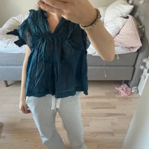 Mörkblå blus från Chelsea - Säljer en luftig mörkblå blus från Chelsea med korta ärmar och v-ringning. Blusen har fina rynkade detaljer vid halsen och är tillverkad i ett lätt material som ger en skön känsla. Perfekt för en avslappnad stil.