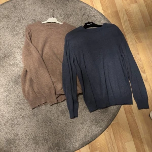 Blå och brun tröja  - Två stilrena tröjor i blått och brunt. Båda tröjorna är långärmade och har en klassisk rund halsringning. Perfekta för kyligare dagar och kan enkelt matchas med olika outfits.