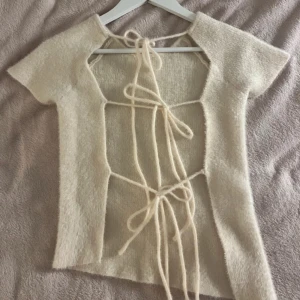 Beige kortärmad topp med snörning - Säljer en snygg topp från Zara med korta ärmar och öppen rygg med snörning. Toppen är mjuk och lite lurvig.