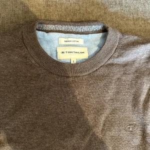 Brun tröja från Tom Tailor - Säljer en stilren brun tröja från Tom Tailor i premium bomull. Tröjan har en rund halsringning och långa ärmar med ribbade muddar. Perfekt för en avslappnad och bekväm stil. Aldrig använd