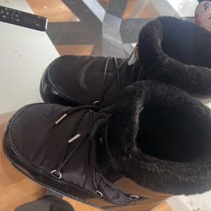 Svarta moon boots med foder - Snygga svarta moon boots med glansig yta och mjukt foder. De har snörning framtill och är perfekta för kalla dagar. Håll fötterna varma och stiliga i vinter!