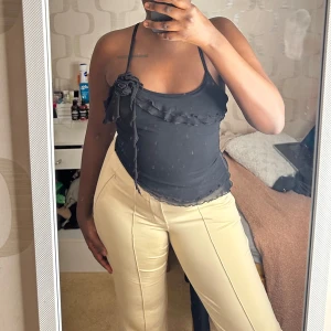 Svart linne med volangdetaljer - Snygg svart linne med smala axelband och volangdetaljer. Toppen har en dekorativ blomma på axeln 🖤