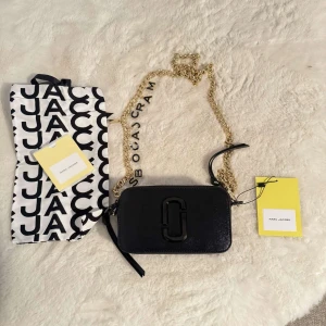 Svart axelväska från Marc Jacobs - Snygg svart axelväska från Marc Jacobs med en elegant guldkedja och märkets logotyp på framsidan. Väskan har en praktisk dragkedja och en stilren design. Oandvänd med prislapp på, köptes för 4 tusen