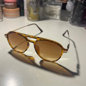 Solglasögon  - Snygga solglasögon med leopardmönstrad båge och bruna tonade glas. De har en klassisk form med dubbel brygga och tunna metallskalmar. Perfekta för en stilren look.