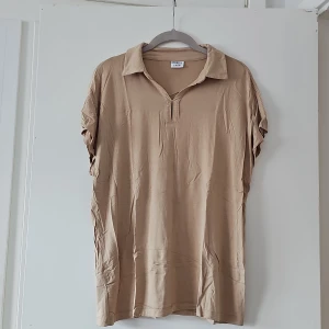 Beige polotopp från Stories - Säljer en stilren beige polotopp från Stories. Toppen har en avslappnad passform med korta ärmar och en klassisk krage. Perfekt för en enkel och chic look.