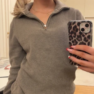 Beige/brun ribbad tröja med dragkedja - Säljer en beige/brun ribbad tröja med dragkedja och krage. Tröjan har långa ärmar och en avslappnad passform, perfekt för en stilren look. Passar bra till jeans eller kjol.