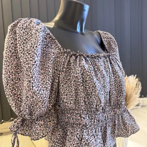 Blommig blus med puffärmar - Säljer en söt blommig blus med puffiga ärmar och knytband vid ärmsluten. Blusen har en elastisk midja och volangdetaljer vid nederkanten. Perfekt för en somrig look! Passar bra som oversize modell (s/m/l storlek). 🌸👌