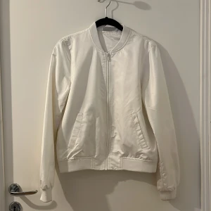 Vit bomberjacka från Noisy May - Säljer en stilren vit bomberjacka från Noisy May. Jackan har en dragkedja framtill och ribbade muddar vid ärmslut och nederkant. Perfekt för en casual look. ❤️Använt max två gånger. Pris kan diskuteras.