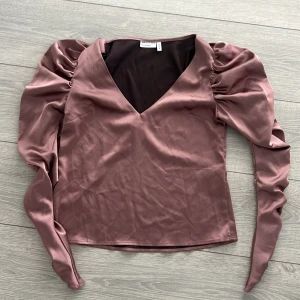 Rosa satinblus från ASOS  - Säljer en elegant rosa blus i satin från ASOS med långa puffärmar och v-ringning. Perfekt för en stilren look.