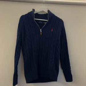 Mörkblå stickad tröja från Polo Ralph Lauren - Säljer en snygg mörkblå stickad tröja från Polo Ralph Lauren med kabelstickat mönster och dragkedja vid halsen. Tröjan är aldrig använd och säljes för den bara legat i garderoben. Den är riktigt bekväm och passar dig som är från 168cm-180cm. Om ni har frågor är det bara att skriva privat!😀