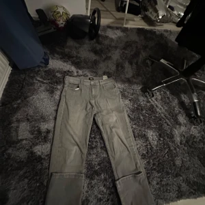 Grå jeans från Lee - Säljer ett par grå jeans från Lee. De har en klassisk design med fem fickor och en normal passform. Modellen på byxorna är slimfit straight, jeansen har en liten defekt i bakre ficka men inget som syns vid användning.storlek är 165-170 cm barn vilket är ungefär 29/30 i vanliga jeans storlekar. Har ni några frågor eller funderingar är det bara att skriva. Mvh Eldin