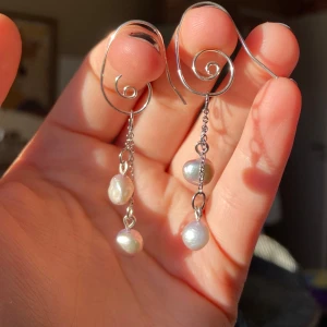 Silvriga örhängen med pärlor - Unika silvriga örhängen med en spiralformad design och hängande kedjor med vita pärlor. Perfekta för att ge en elegant touch till din stil. 