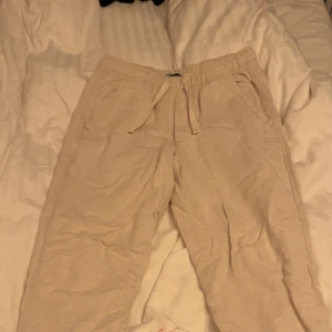Beige linnebyxor med snörning - Säljer ett par bekväma beige linnebyxor med elastisk midja och snörning. Perfekta för en avslappnad stil. Byxorna har fickor på sidorna och en lös passform.