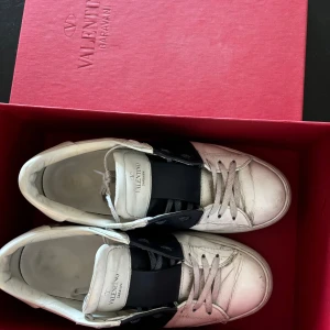 Valentino sneakers - Snygga Valentino Garavani sneakers i vitt med svarta detaljer. Skorna har snörning och en rund tå, vilket ger en klassisk look. Perfekta för dig som vill ha stil och komfort i ett.