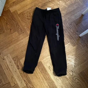 Svarta mjukisbyxor från Champion - Säljer ett par svarta mjukisbyxor från Champion med logotypen tryckt längs benet. Byxorna är tillverkade i en mjuk bomullsblandning och har en elastisk midja för extra komfort.