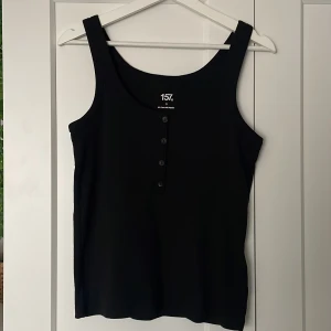 Svart linnetopp från 157 - Snygg svart linnetopp från 157 med knappar framtill. Tillverkad i en mjuk blandning av bomull och polyester. Perfekt för en stilren look.