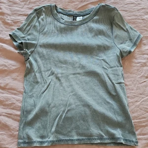 Grön ribbad t-shirt från H&M Divided - Säljer en stilren grön ribbad t-shirt från H&M Divided. Den har en klassisk rund hals och korta ärmar, perfekt för en avslappnad look. Passar bra till jeans eller shorts för en casual stil. 🌿