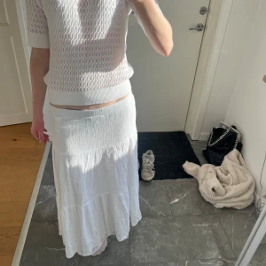 Vit långkjol lågmidjad - Säljer en vit långkjol med en luftig och flödande design. Kjolen har en elastisk midja och är perfekt för varma dagar. Den är tillverkad i ett lätt material som ger en skön känsla.
