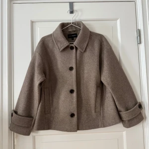Beige kappa från KappAhl - Säljer en stilren beige kappa från KappAhl i storlek M. Jackan har en klassisk krage och knäpps med stora knappar framtill. Den är tillverkad i en mjuk polyesterblandning och har uppvikta ärmslut för en extra touch. Beige jacka från Kappahl. Två fickor. Använd ett fåtal gånger. Kan finnas några noppror. Upptäckte nu ett märke på ryggen (se bild), går troligtvis att tvätta bort. Storlek M. Normal i storlek. 