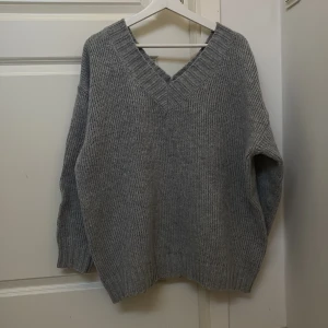 Grå stickad tröja - Säljer en mysig grå stickad tröja med v-ringning. Tröjan är tillverkad i 100% polyester och har långa ärmar. Perfekt för kyliga dagar. Tröjan hade ingen lapp där märket står så det vet jag dessvärre inte.