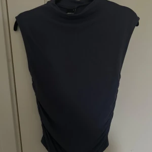 Mörkblå topp  - Snygg mörkblå topp från Gina Tricot med en stilren design. Klänningen har en normal passform och är ärmlös, vilket gör den perfekt för olika tillfällen. Tillverkad i ett mjukt och bekvämt material.