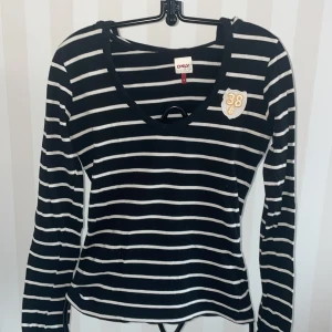 Svart och vit randig tröja från ONLY nyskick  - Säljer en svart och vit randig tröja från ONLY med ett coolt märke med siffran 38 på bröstet. Tröjan har en v-ringad hals och långa ärmar, perfekt för en avslappnad stil. Passar bra till jeans eller kjol för en casual look.