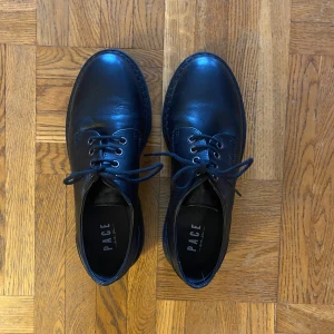 Svarta snörskor från PACE - Snygga svarta snörskor från PACE i skinn. De har en rund tå och robust sula, perfekt för en stilren look. Skorna har klassisk snörning och en elegant design som passar till många tillfällen. Knappt använda. Köpta för 400 kr, säljer för 250 kr.