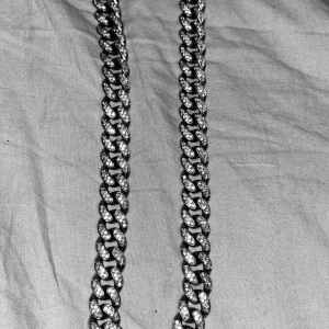 Iced out silver cuban halsband - Säljer ett chunky cuban chain halsband i silverfärg med glittrande stenar på varje länk. Kedjan har en bred och tung look som verkligen sticker ut och ett lås dekorerat med stenar för extra bling. Perfekt för dig som vill ha en statement piece.