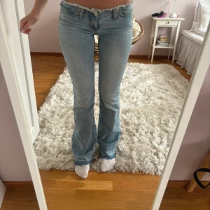 Ljusblå bootcut jeans låg midja - Säljer ett par ljusblå jeans med bootcut-modell och låg midja. Jeansen har klassisk femficksdesign, dragkedja och knapp framtill. Perfekta för dig som gillar en avslappnad och trendig look med lite retrovibbar. Materialet är jeans i bomull.