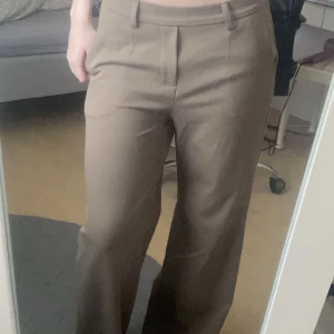 Beiga wide kostymbyxor från Object - Snygga beiga kostymbyxor från Object i storlek 36. Byxorna har hög midja(funkar även som lågmidjat), resår baktill, vida ben och pressveck framtill. De har även två prydnadsfickor bak. Byxorna är en aning långa på mig som 171cm lång, samt att de är lagade nertill på ena benet då sömmen lossnat en gång, syns dock knappt!(se bild)💕