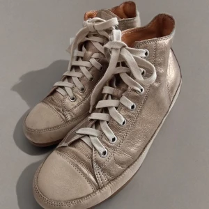 L’Ecologica högsko i metallic - Snygga och bekväma high-top sneakers i metallicläder från L’Ecologica - Made in Italy. Tillverkade i Italien med mjukt läder och diskret glans. Passar perfekt till jeans, klänning eller mer avslappnade byxor. Skick: Varsamt använda, naturliga veck i lädret (se bild), sulor i fint skick  Färg: Champagne/guld (ljus metallic)  Material: Äkta läder ovandel och foder, gummisula  Märke: L’Ecologica (präglad sula)