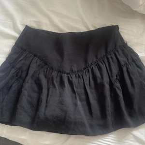 Svart volangkjol från Zara - Supersöt svart kortkjol från Zara med volang och bred midja. Kjolen är i ett lätt och flowy material som ger en snygg siluett. Perfekt att styla med en croppad topp eller oversized hoodie för en chill vibe.