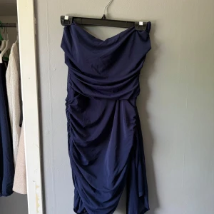 Marinblå draperad kortklänning - Snygg marinblå kortklänning med draperad design och offshoulder-stil. Klänningen har en tight passform och är tillverkad i ett mjukt, lätt material. Har använt den 1 gång och är annars i nyskckt. Säljer pågrund av att den inte kommit till användning mer.