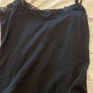 Svart linnetopp med spets från Esmara - Svart linnetopp från Esmara med tunna axelband och snygg spetskant upptill. Toppen är i mjuk bomullsmix med lite stretch för skön passform. Perfekt för lager på lager eller som statement-piece till jeans eller kjol.