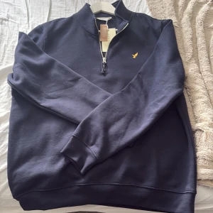 Mörkblå half zip tröja från Pier One - Snygg mörkblå tröja från Pier One med halv dragkedja och gul broderad logga på bröstet. Tröjan har hög krage och är tillverkad i mjuk bomullsmix. Perfekt för lager-på-lager och chill vardagsstil.