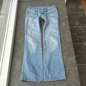 Lågmidjade diesel jeans - Säljer ett par ljusblå lågmidjade jeans från Diesel med låg midja. Jeansen har dubbla knappar i midjan, stora framfickor och klassiska bakfickor med röd Diesel-detalj. Tillverkade i jeansmaterial och har en snygg pass form både bak och fram. Finns ett litet hål i sömnen vid midjan men syns knappt. Måtten på jeansen:  Innerbenslängd är: 79cm, midjemått är:39cm, midjehöjden är :19 cm💞💞