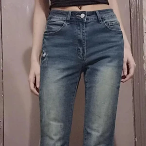 Blå bootcut jeans med broderade fickor - Snygga blå bootcut jeans med hög midja och coola broderade detaljer på bakfickorna. Jeansen har klassisk femficksdesign, knappstängning och är tillverkade i jeansmaterial. Perfekta för dig som vill sticka ut med unika detaljer på dina byxor.