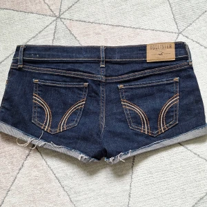 Low waist jeansshorts hollister - Snygga mörkblå jeansshorts från Hollister med klassiska bakfickor och kontrastsömmar. Modellen har låg midja, uppvikta ben och råa kanter för en avslappnad vibe. Perfekta för sommardagar och enkel att matcha med allt. Säljer pga att de inte passade som jag ville! Annars jätte fina