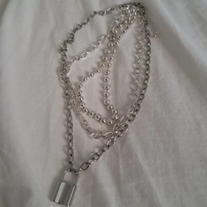 Chunky layered silverfärgat halsband med lås - Trendigt lager-på-lager halsband i silverfärg med grova kedjor, kulkedja och ett coolt hänglås som detalj. Perfekt statement piece för att lyfta din outfit. Metallkedjorna ger en edgy vibe och passar dig som gillar att sticka ut. Kedjan med hänglås sitter inte ihop med de andra halsbanden så den kan bäras ensam om man vill det.